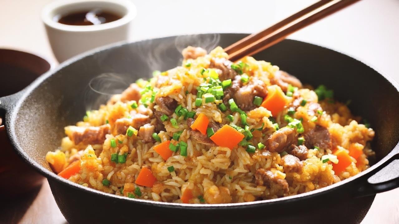 Golden-brown mixed meat fried rice piled high in a carbon steel wok, with visible chunks of chicken, beef, and pork; scrambled eggs; and diced carrots. Topped with sliced green onions, with a pair of wooden chopsticks resting on the wok’s edge. Warm, appetizing色调—sunlight hits the rice, making it glisten. Background is a white kitchen counter with a small bowl of soy sauce. Mouthwatering, homey vibe.